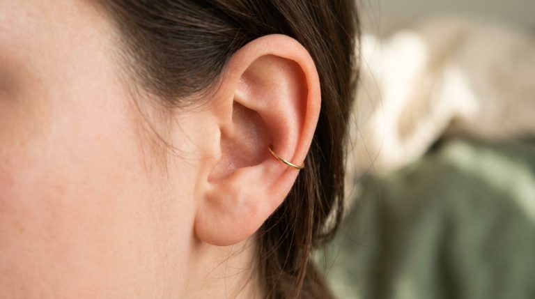 Gros plan sur une oreille avec un piercing conch discret : un anneau doré élégant et moderne. Cheveux foncés.