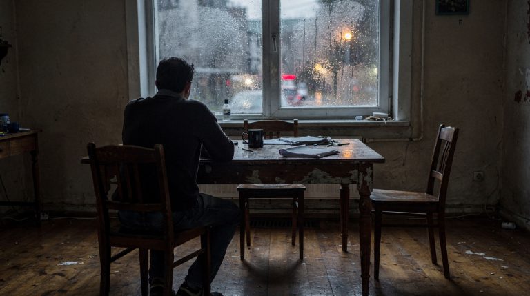 Homme pensif assis seul près d'une fenêtre le soir