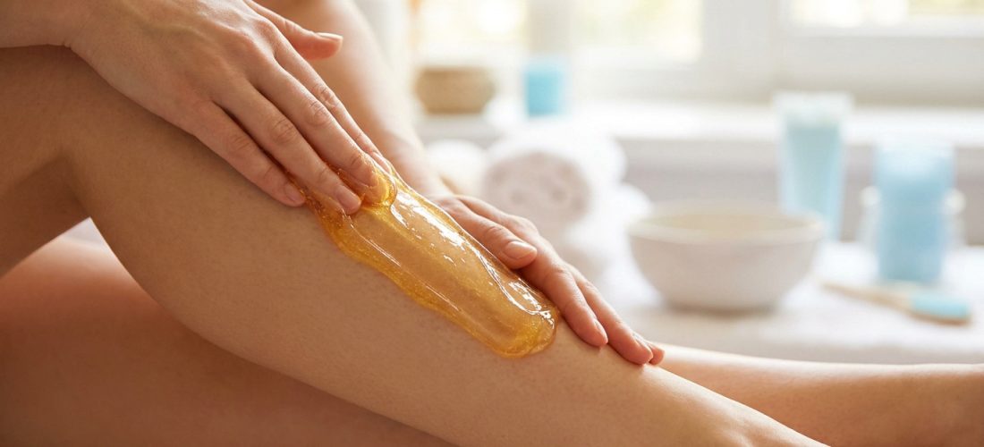 Une femme applique de la pâte à sucre dorée sur sa jambe pour une épilation naturelle.