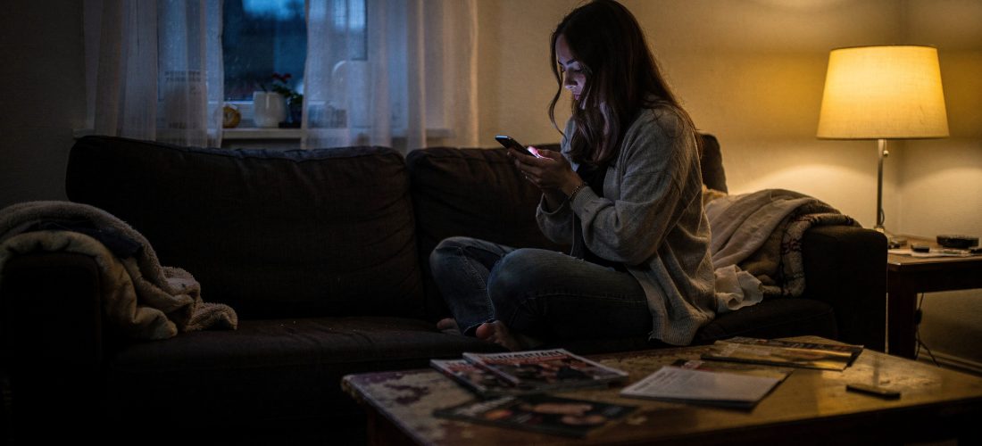 Femme seule sur un canapé regardant son téléphone avec inquiétude