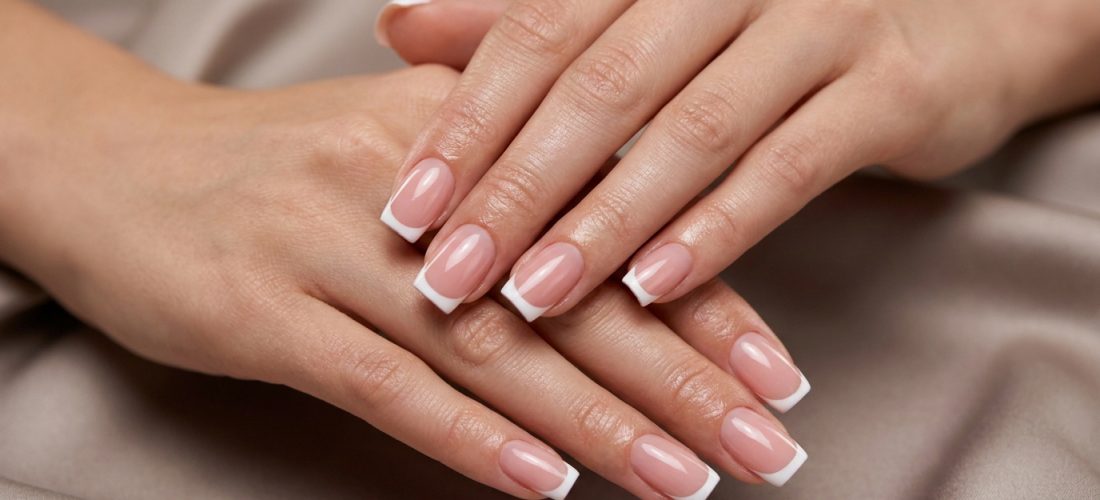 Gros plan sur deux mains féminines aux ongles manucurés avec un style français carré blanc et rose naturel, posées sur un tissu satiné.