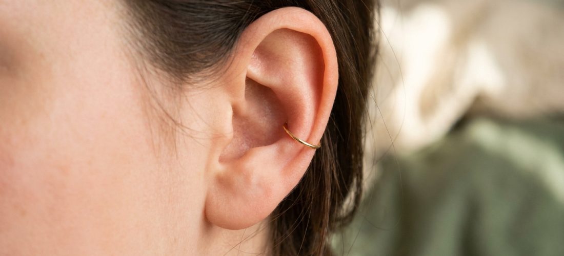 Gros plan sur une oreille avec un piercing conch discret : un anneau doré élégant et moderne. Cheveux foncés.